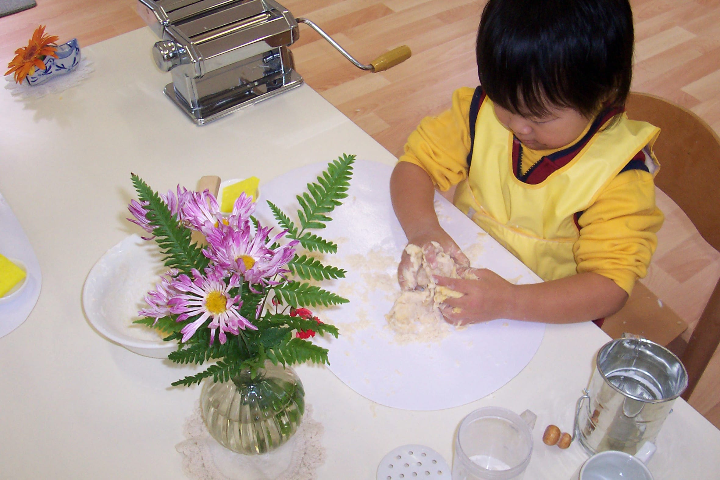 A young Montessori child in Australia at a practical-life work station, kneading dough beside a small flower arrangement.
