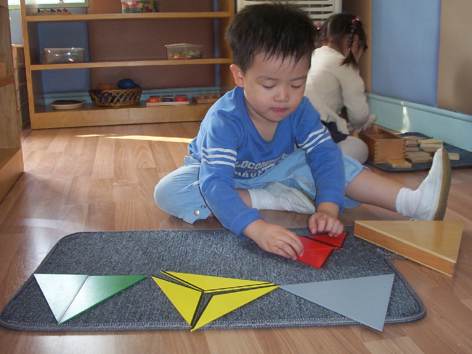 A young child in a Montessori classroom in Japan working with the constructive triangles on a floor mat.