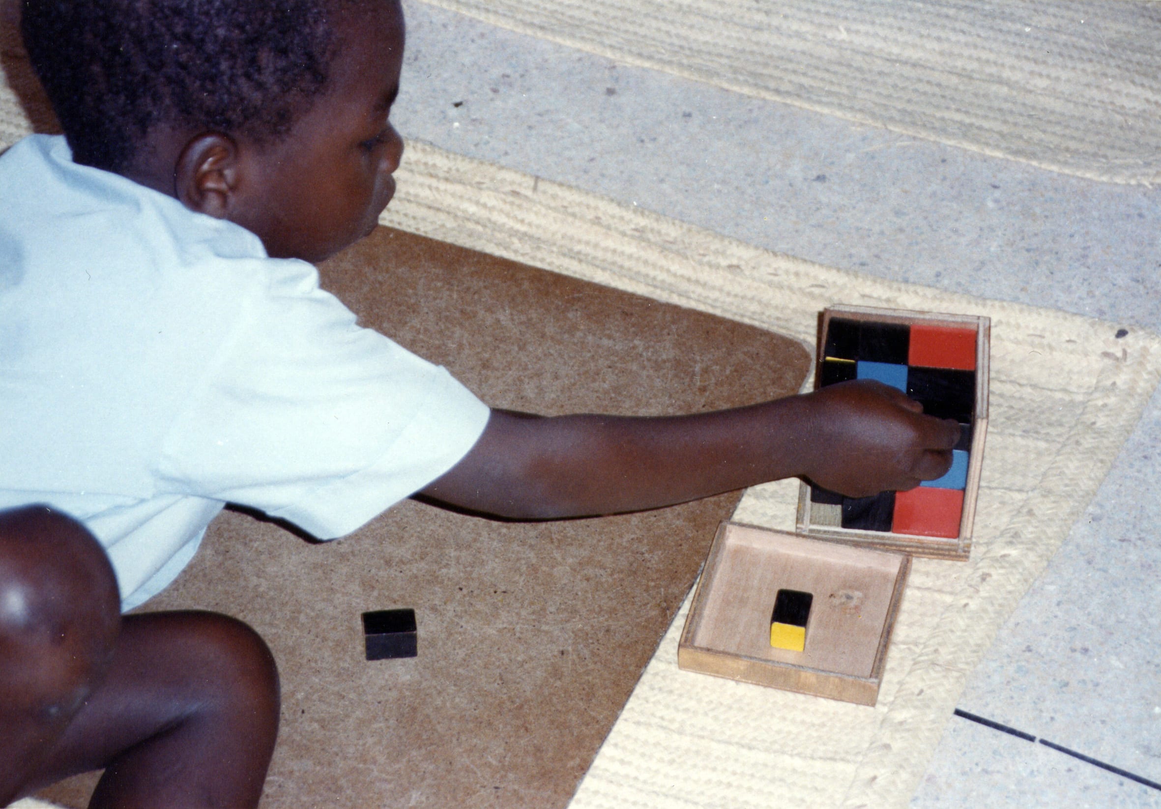 A child in a Montessori classroom in Tanzania assembling a binomial cube.