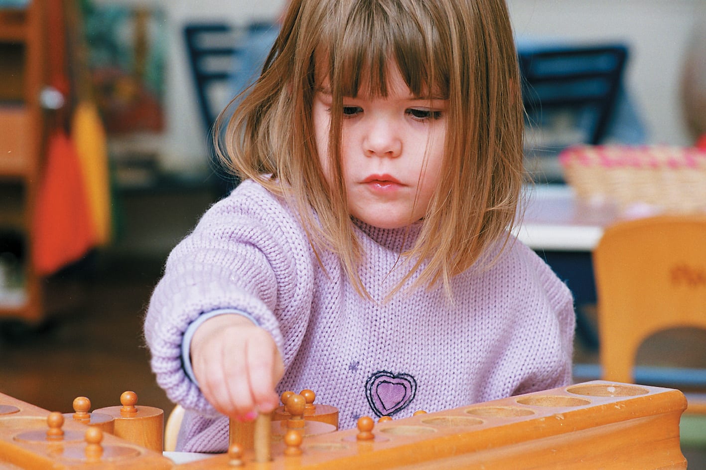 A young child in a Montessori classroom in the United Kingdom concentrating on the knobbed-cylinders work.