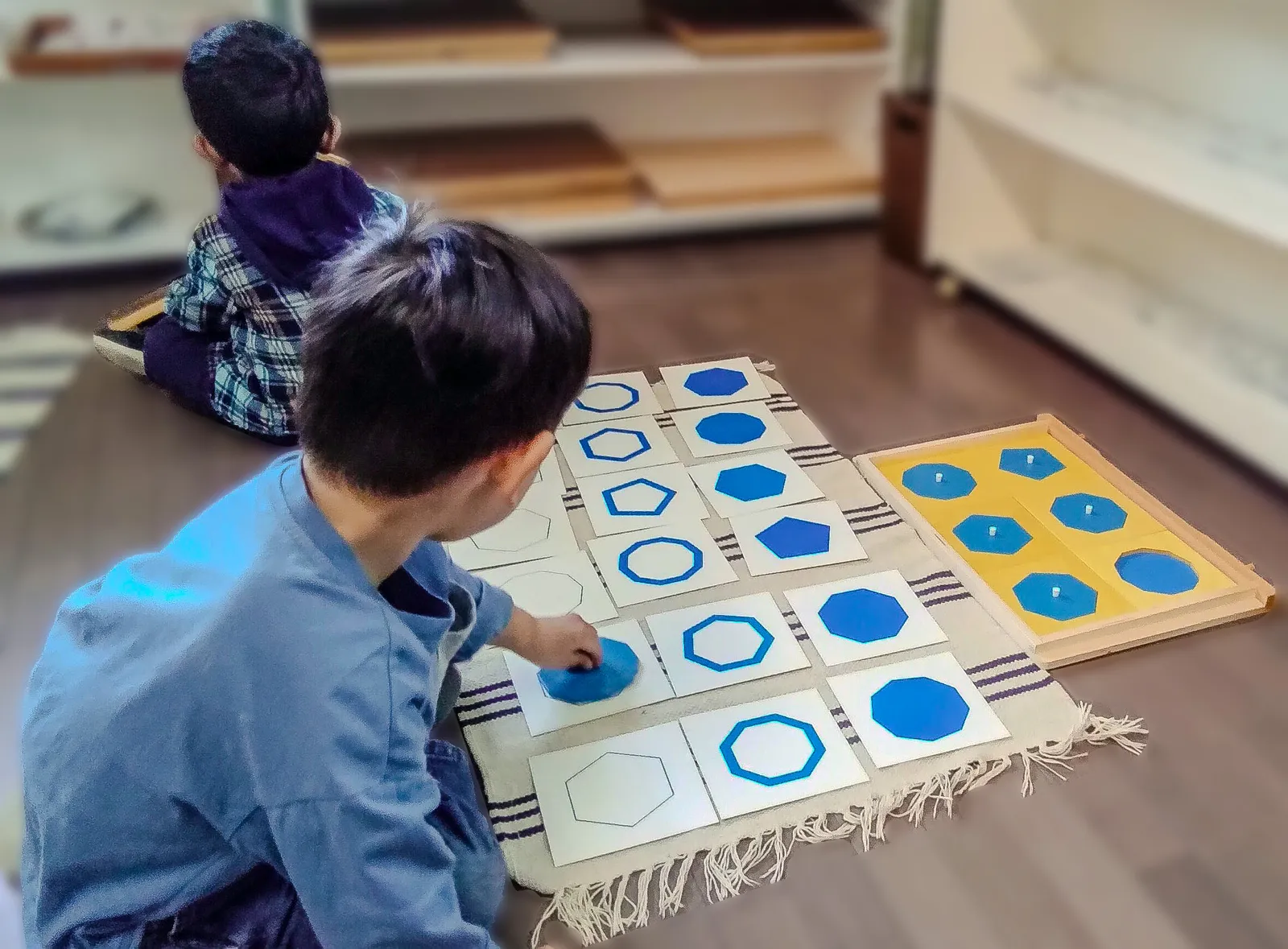 A child matching geometric shapes on a work mat in the Casa classroom.