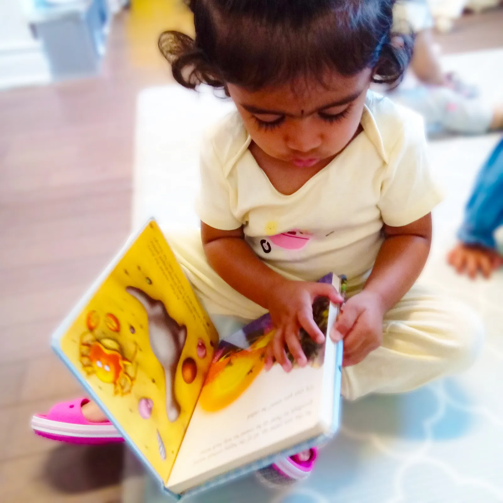 A toddler absorbed in a picture book at ACE Montessori.