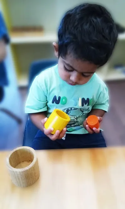 A toddler handling small wooden cylinders at ACE Montessori.